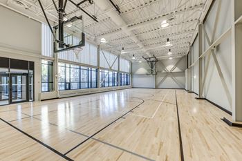 A basketball court inside a gym with wooden floors and a basketball hoop.